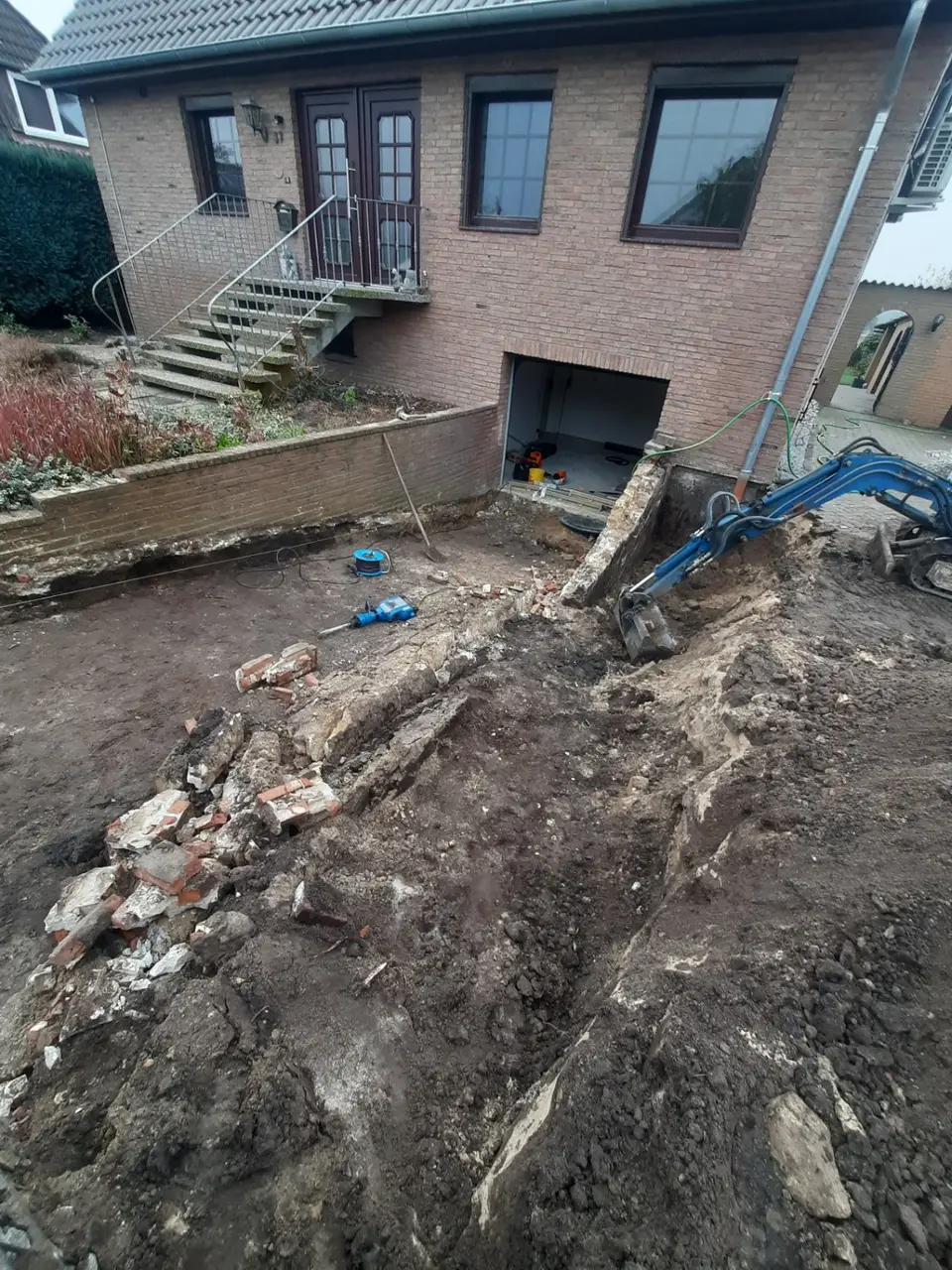 Minibagger beim Rückbau einer Mauer und alter Fundamente vor einem Wohnhaus