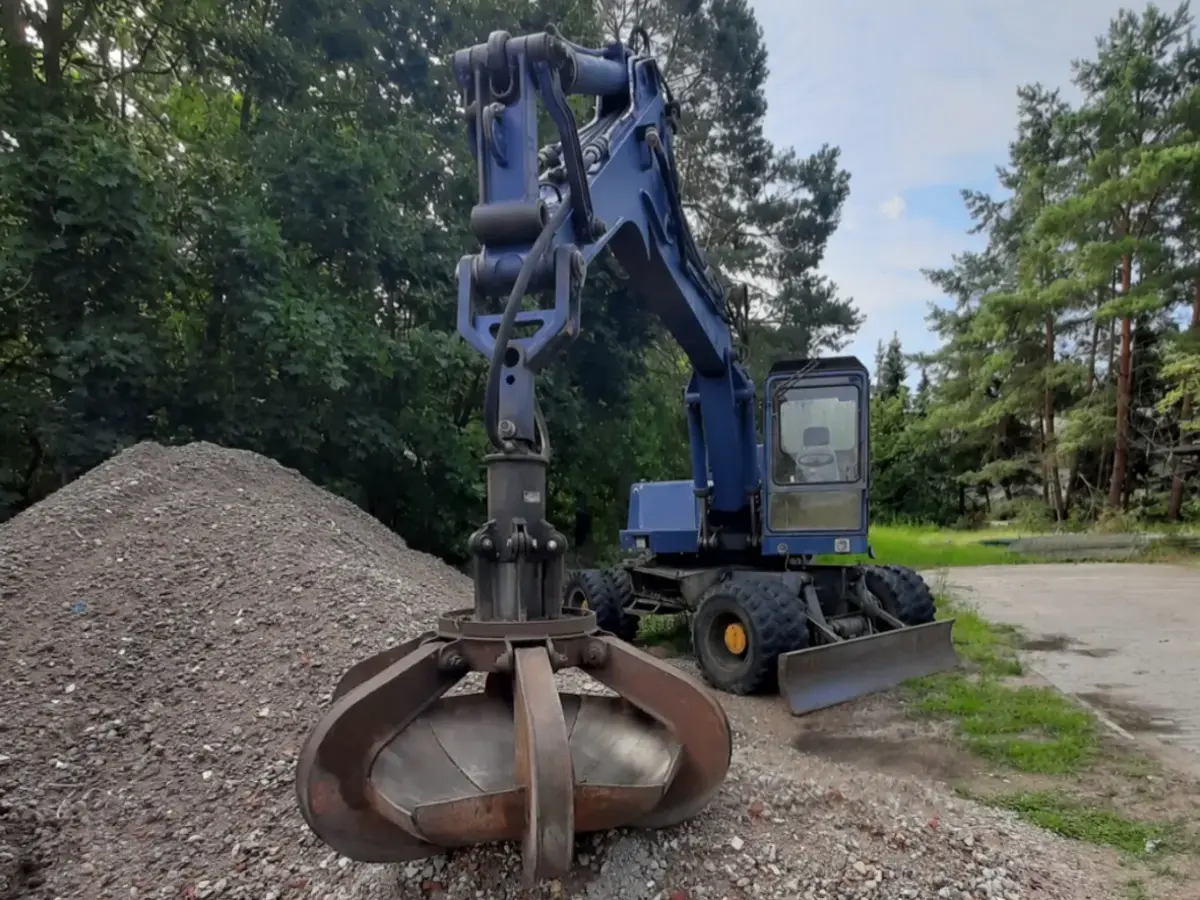 Blauer Mobilbagger mit Greifer vor gelagertem Mineralgemisch