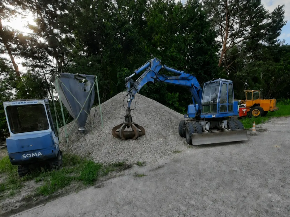 Blauer Mobilbagger mit Greifer an einem Mineralhaufen