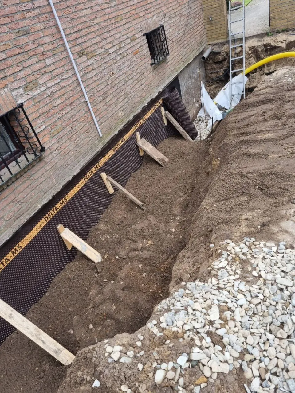 Vorbereiteter Drainagestreifen mit Filterkies entlang einer abgedichteten Hauswand