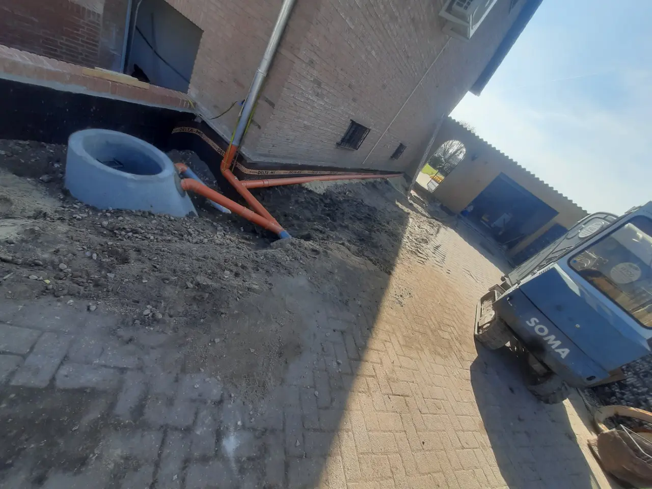 Mehrere Entwässerungsleitungen führen entlang eines Gebäudes zu einem Betonschacht