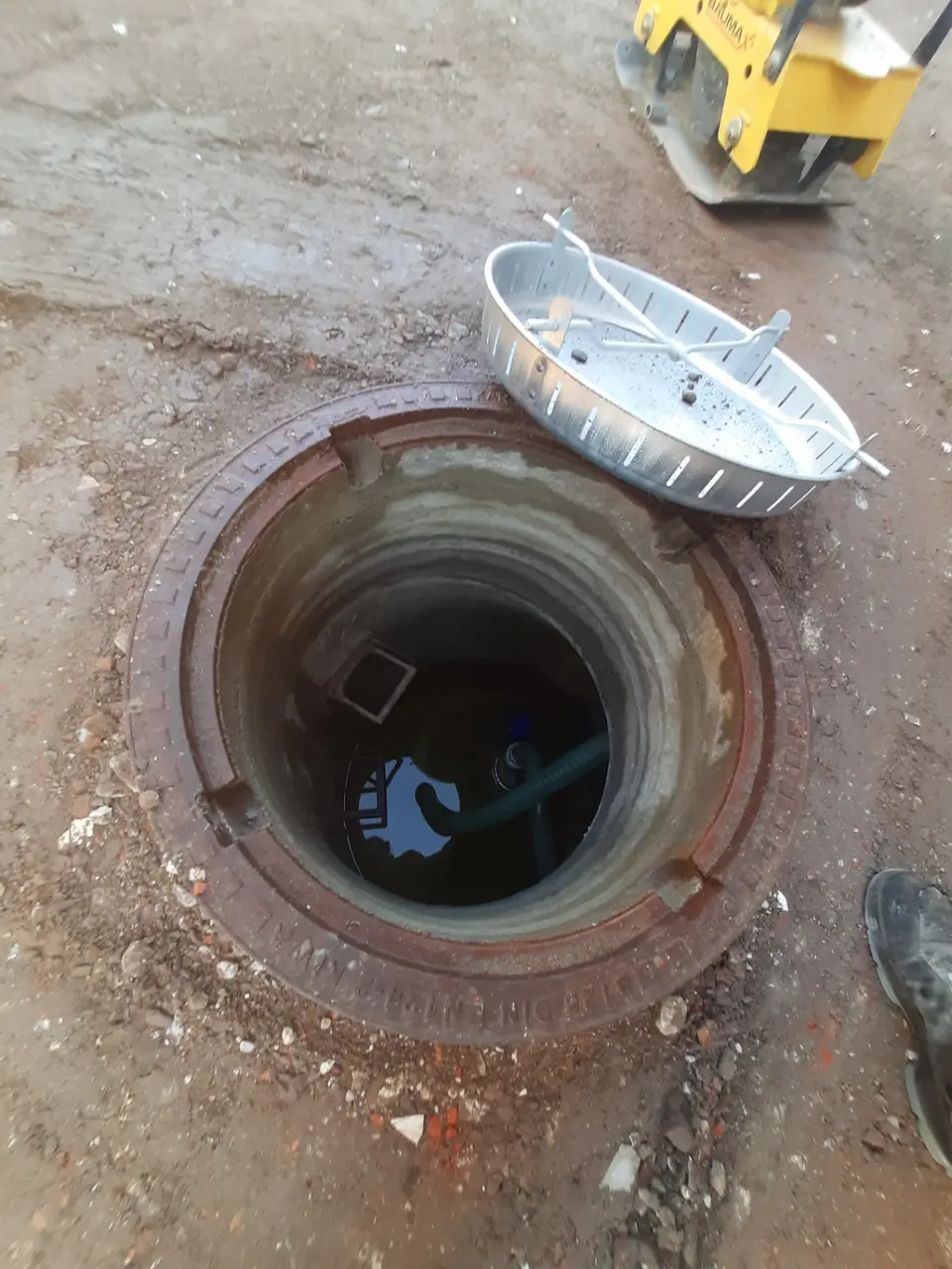Geöffneter Betonschacht mit Wasser und Pumpenschlauch während der Bauarbeiten