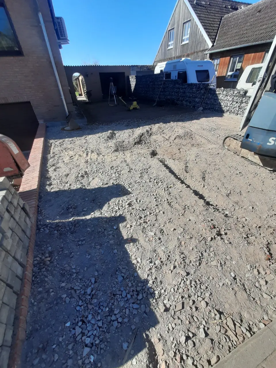 Großflächig vorbereitete Grundstücksfläche mit eingebrachtem Mineralgemisch und Bagger am Rand