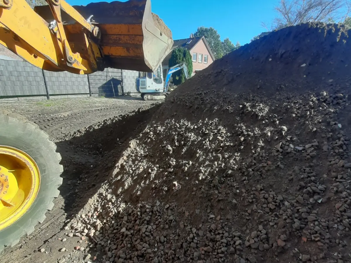 Großer Haufen aus Boden und Mineral mit Schaufel eines Radladers und Bagger im Hintergrund