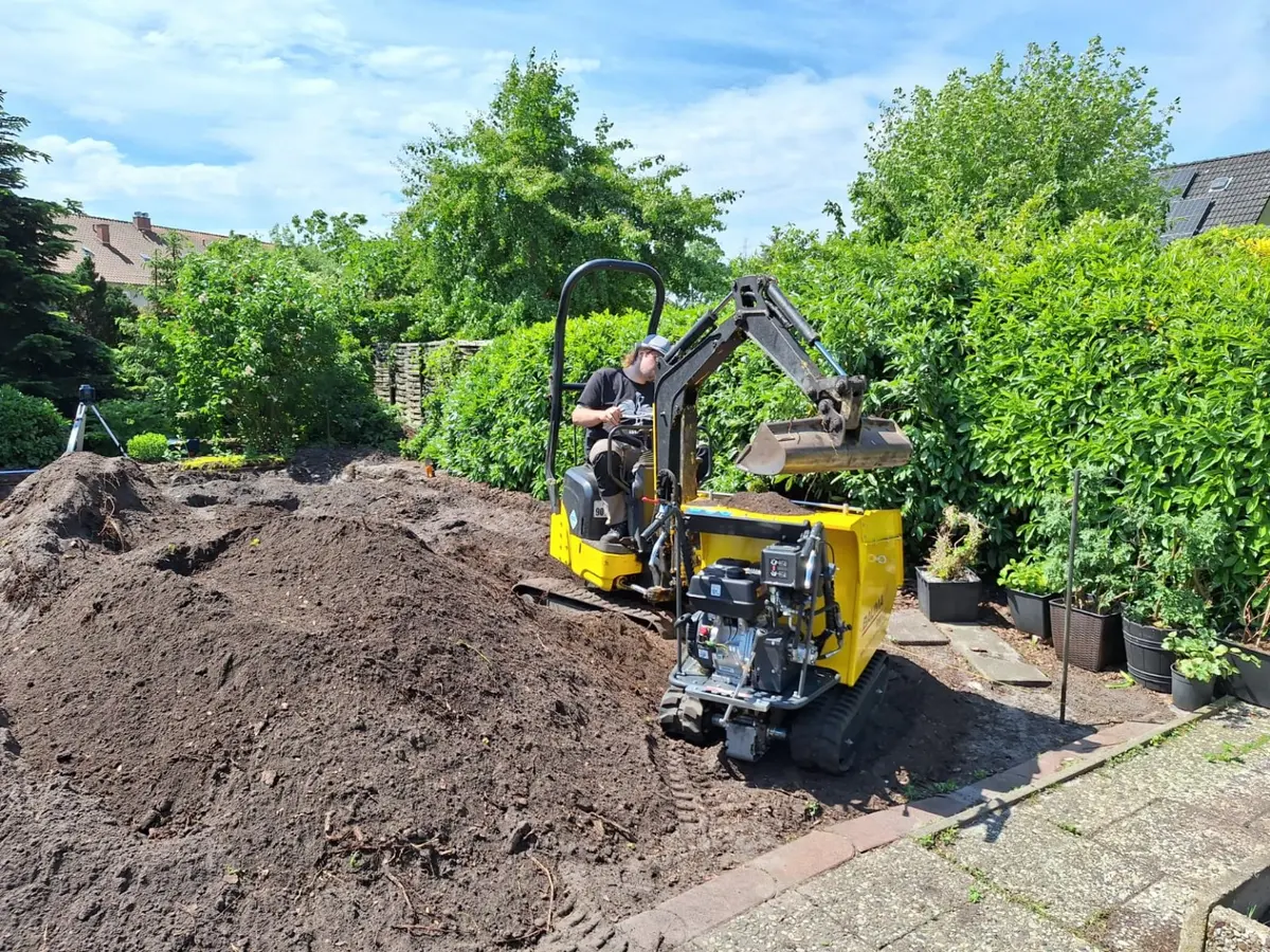 Minibagger belädt einen Kettendumper bei Erdarbeiten auf engem Privatgrundstück