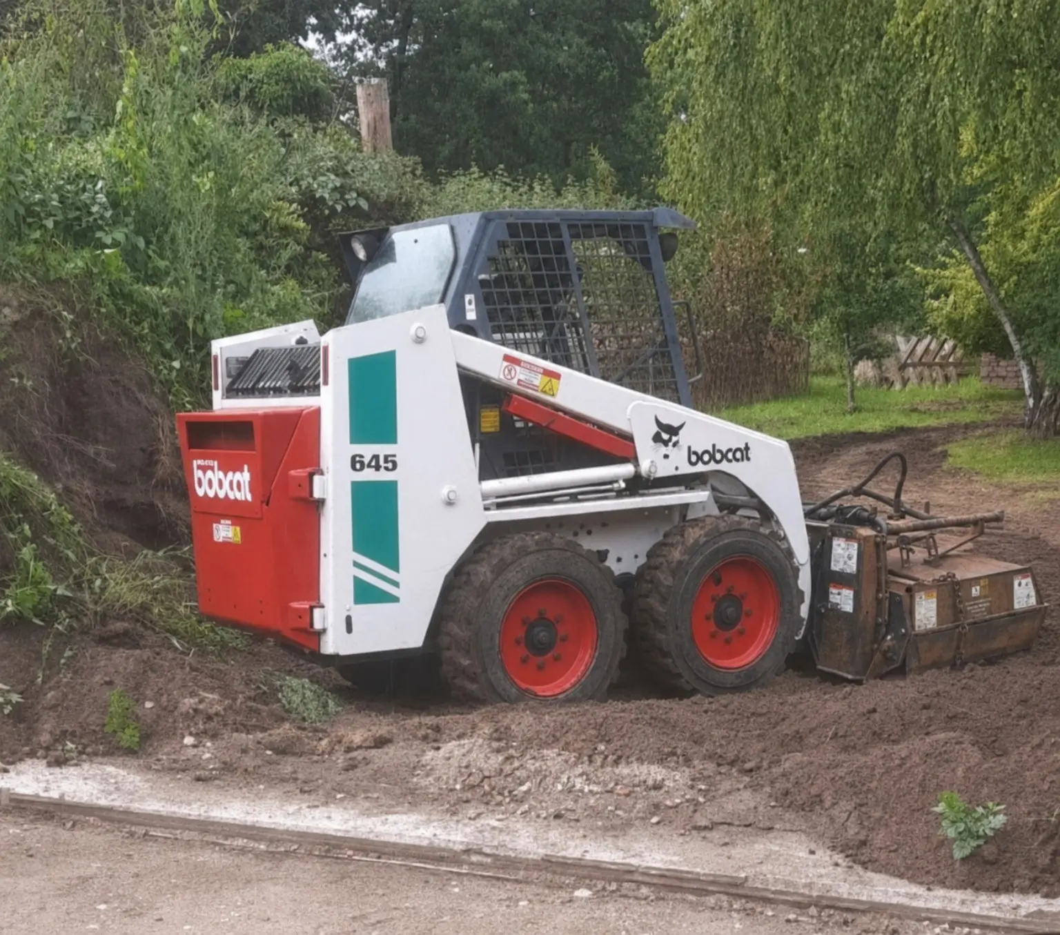 Bobcat-Kompaktlader 645 mit Bodenfräse bei der maschinellen Bearbeitung einer Gartenfläche
