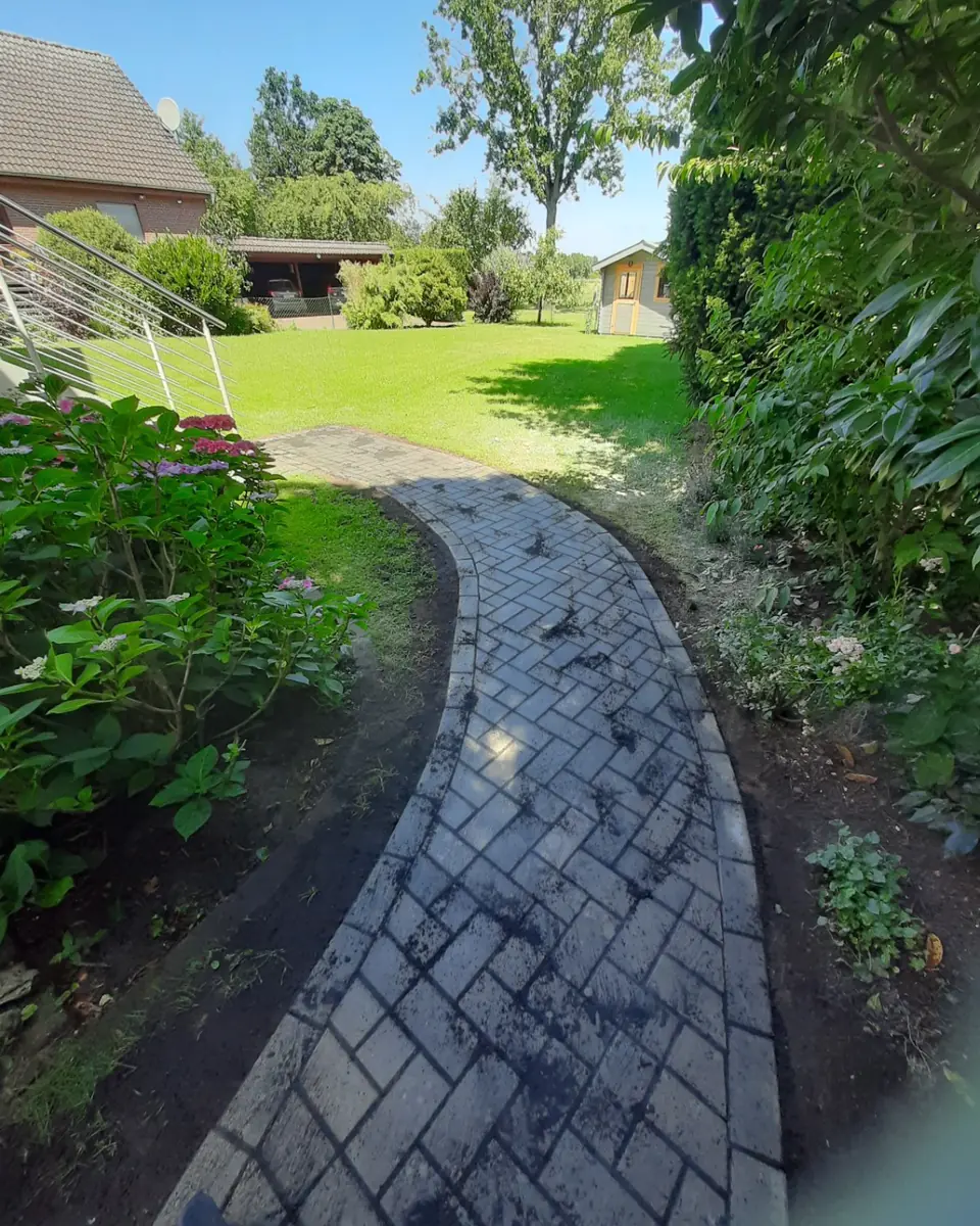 Fertiggestellter geschwungener Gartenweg mit grauem Pflaster und sauberer Randeinfassung