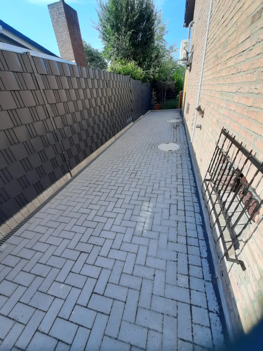 Langer fertig gepflasterter Seitenweg zwischen Hauswand und Sichtschutz