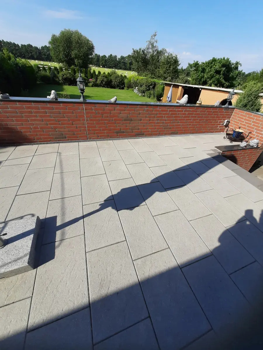 Großzügige Terrasse aus hellen rechteckigen Platten mit Entwässerungsrinne an einer Ziegelmauer