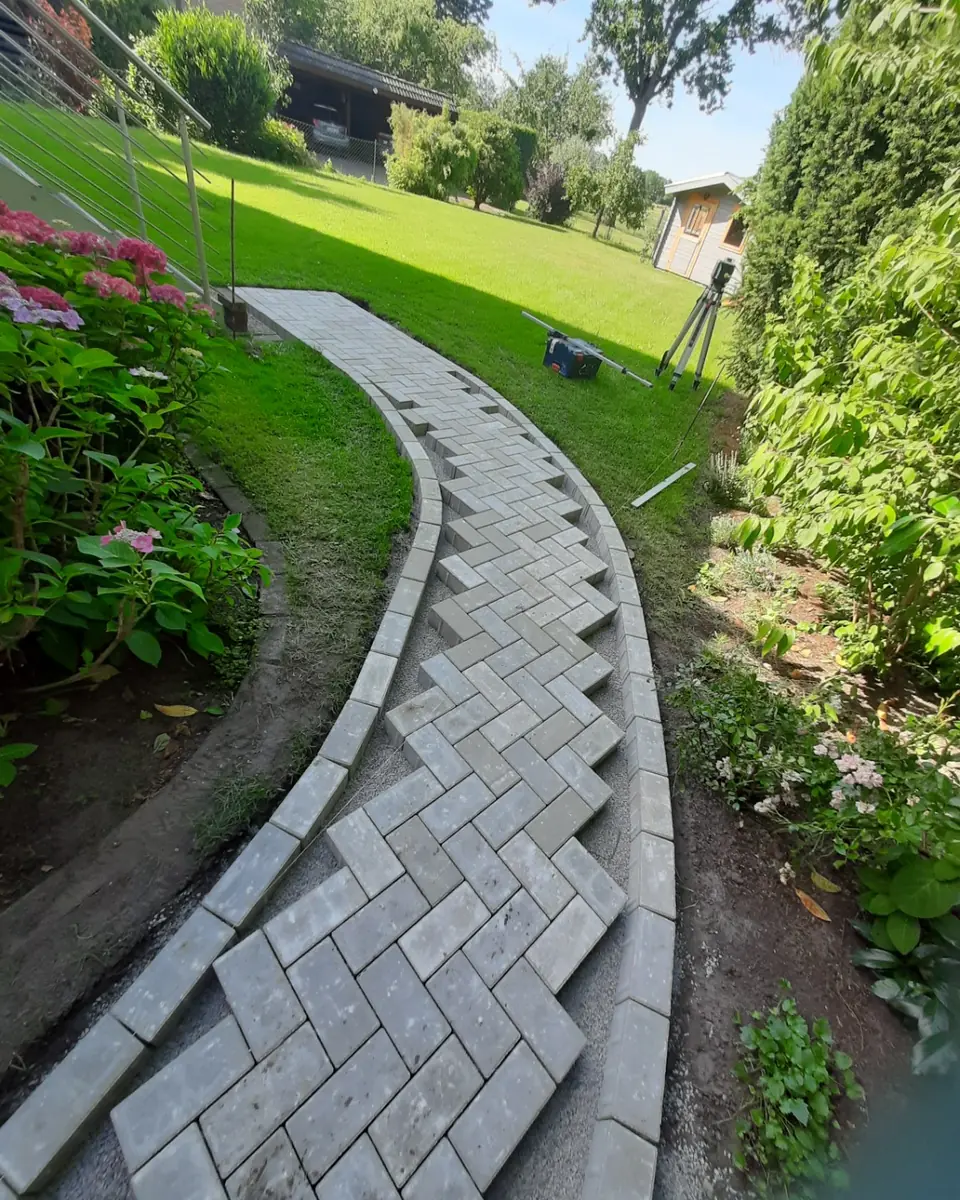 Geschwungener Gartenweg während der Verlegung von grauen Rechteckpflastersteinen